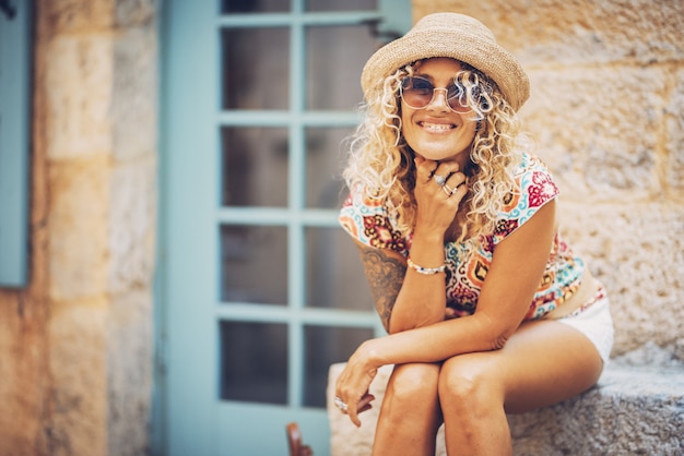 Photo portrait of beautiful smiling hipster young woman in sunglasses and straw hat sitting outdoors on a bright sunny day. stylish tattooed woman in good mood spending leisure time