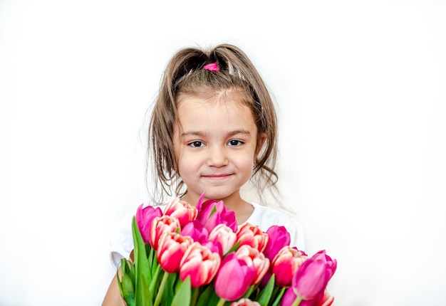 Портрет красивой улыбающейся маленькой девочки с весенними тюльпанами на белом фоне