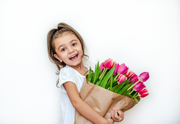 Portrait of a beautiful smiling little girl with spring tulips on a white background