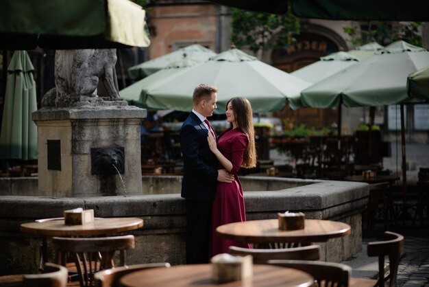 Portrait of beautiful smiling love couple sitting near fountain outdoors in the city.