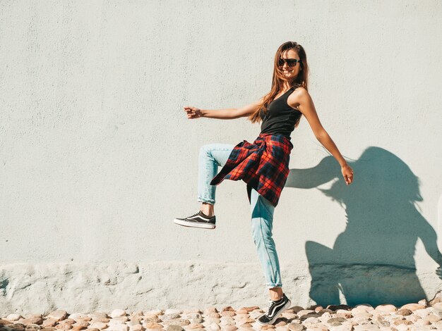 Portrait of beautiful smiling model. female dressed in summer hipster checkered shirt and jeans. she posing near wall in the street