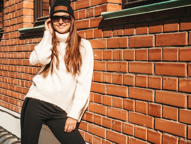 Portrait of beautiful smiling model. Female dressed in warm hipster white sweater and beanie. Posing in the street