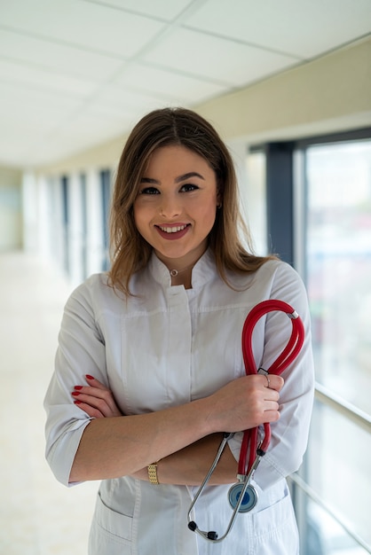 Ritratto di bella infermiera sorridente in uniforme bianca con lo stetoscopio che guarda l'obbiettivo e sorridente. studente di medicina