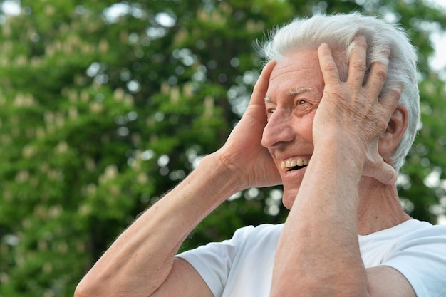 Портрет красивого улыбающегося пожилого мужчины, позирующего в летнем парке