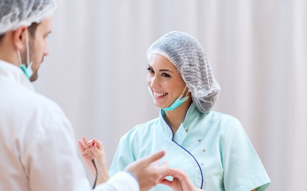 Portrait of beautiful smiling in uniform, medical cap and with protective mask talking to doctor after successful surgery.