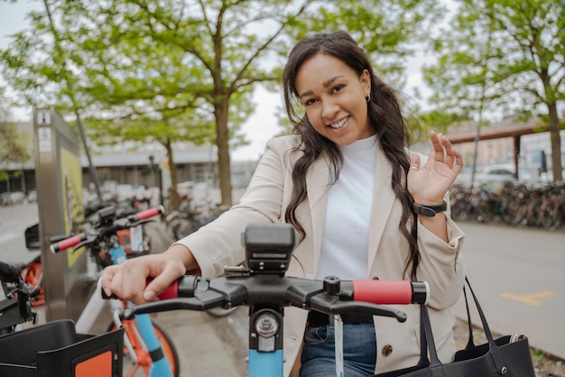 Portrait of beautiful smiling woman salutation, riding on electric scooter on the street