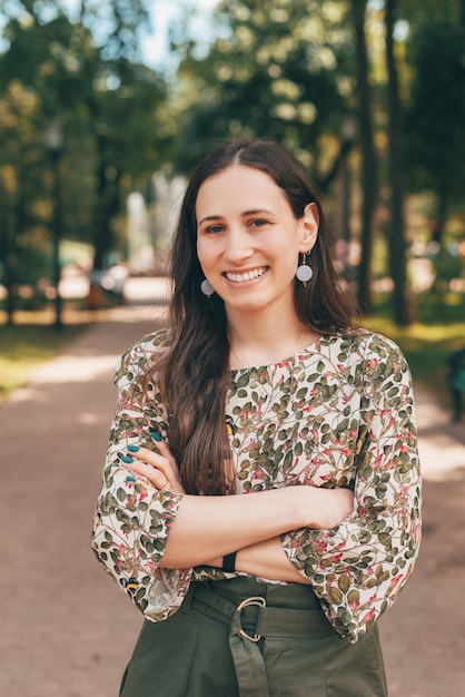 Portrait of beautiful smiling woman with crossed arms in park