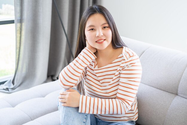 portrait of beautiful smiling young asian woman with long dark hair in striped longsleeve at home