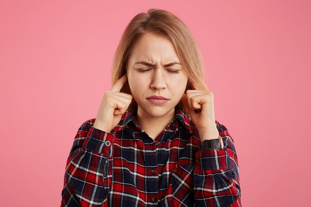 Portrait of beautiful stressful female closes eyes in panic and plugs ears