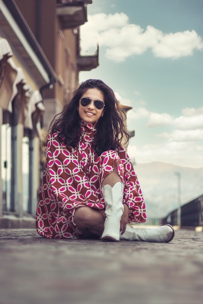 Portrait of a beautiful stylish woman posing sitting down on the street