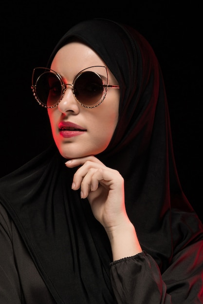 Portrait of beautiful stylish young muslim woman wearing black hijab and sunglasses as modern eastern fashion concept posing