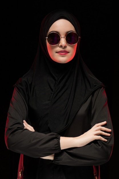 Portrait of beautiful stylish young muslim woman wearing black hijab and sunglasses as modern eastern fashion concept posing