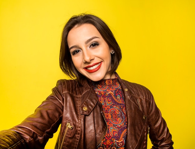 Portrait of a Beautiful successful smiling woman doing selfie on a yellow wall