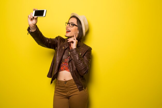 Portrait of a beautiful successful smiling woman doing selfie on a yellow wall