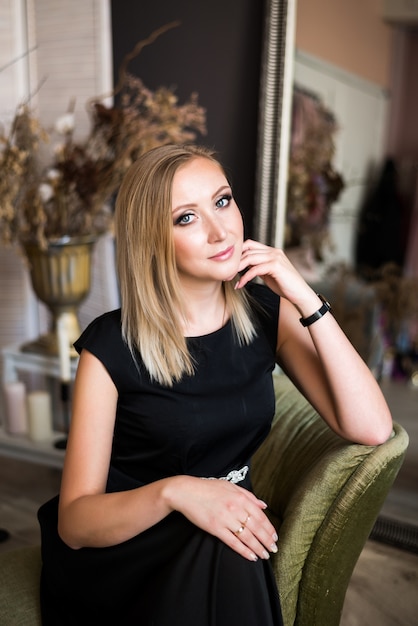 Portrait of a beautiful successful young blonde woman with professional makeup. woman in a black dress posing sitting