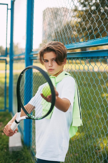 Foto ritratto di un bel ragazzo adolescente in piedi con una racchetta da tennis e una palla nelle mani