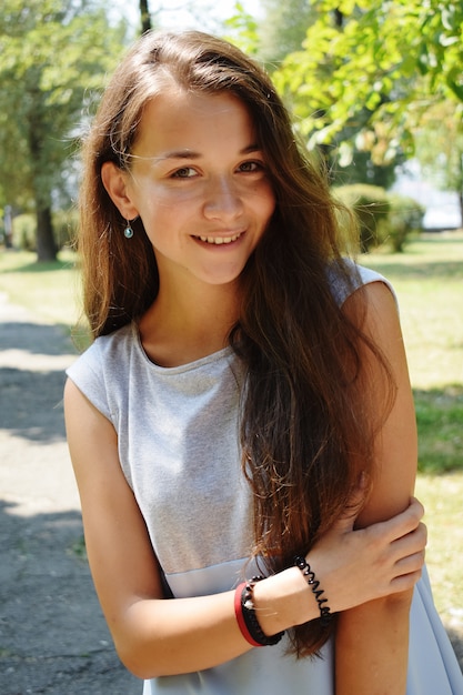 Photo portrait of beautiful teenage girl in blue blouse, against green of summer park play with her hair.