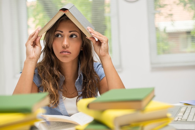 Portrait of beautiful teenage girl holding book above head and bored of a learning.