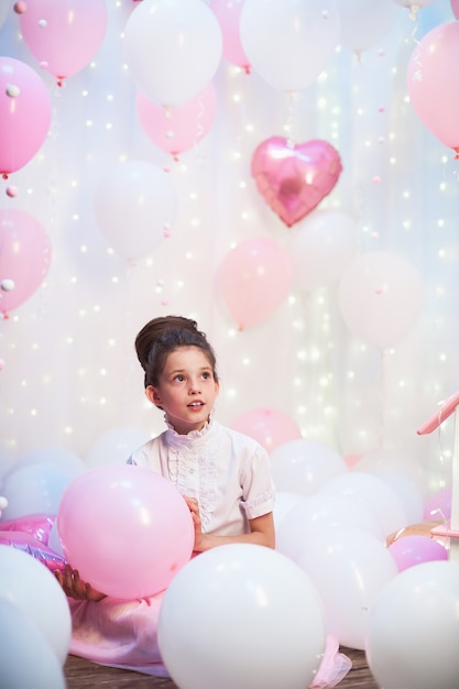 Ritratto di una bella ragazza adolescente in una lussureggiante gonna rosa nello scenario di palloncini palloncini in lattice e foil riempiti con elio.