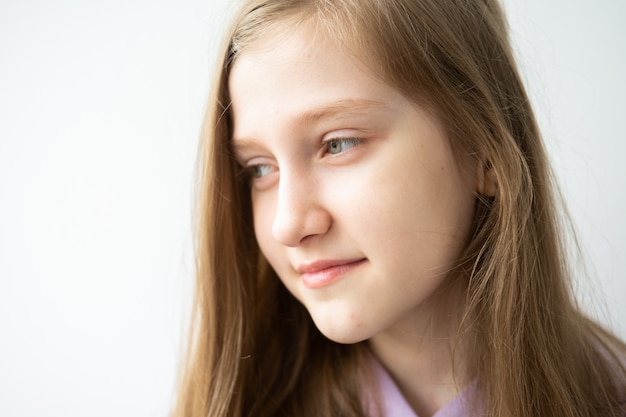 Photo portrait of beautiful teenage girl with long hair in purple hoodie standing against white wall.