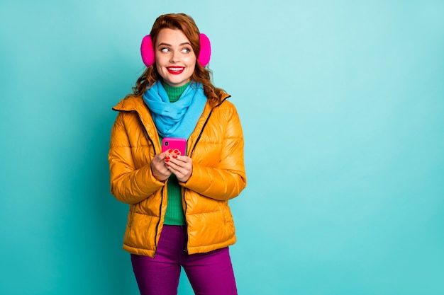 portrait of beautiful traveler lady hold telephone look interested side empty space wear trendy casual yellow overcoat scarf purple pants.