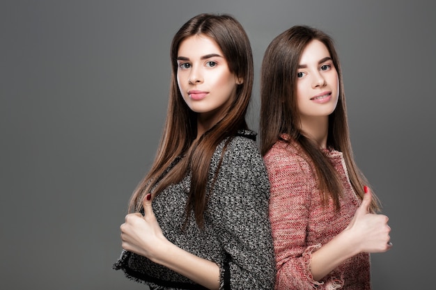 Portrait of beautiful twins women showing gesture thumbs up