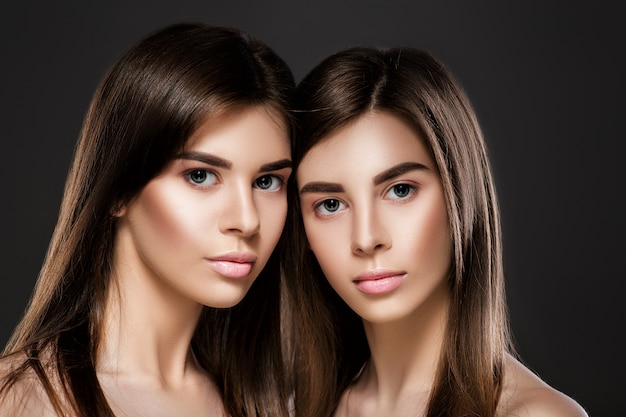 Портрет красивых женщин-близнецов с идеальной кожей, естественным макияжем и длинными волосами. мода