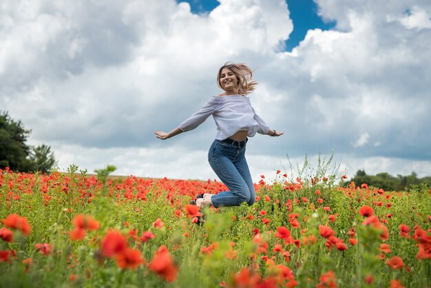 Portrait of beautiful ukrainian woman with blond hair, wearing white blouse, posing in poppy field at sunny day, lifestyle