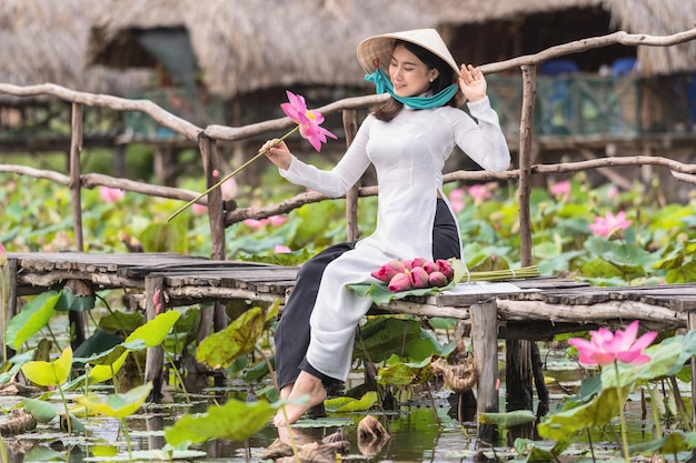 Портрет красивой вьетнамской женщины в традиционной вьетнамской шляпе, держащей розовый лотос