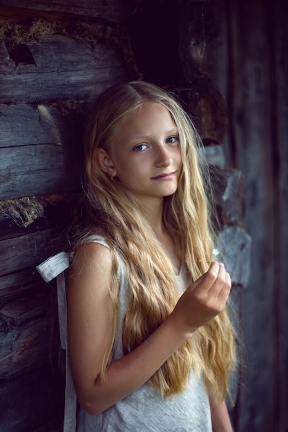 여름에 나무 오래된 헛간 옆에 앉아 드레스와 모자에 긴 머리를 가진 아름다운 마을 소녀 금발의 초상화