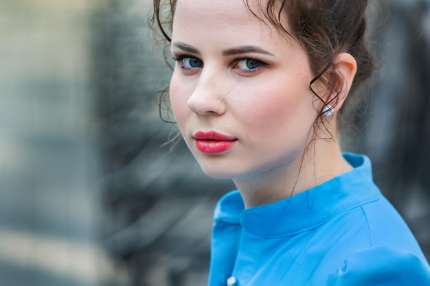 Portrait of a beautiful white European brunette girl wearing a blue dress on the street in the summe