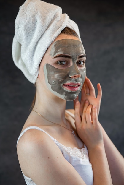 Portrait of beautiful Woman applying nourishing green clay mud mask to her face isolated on black