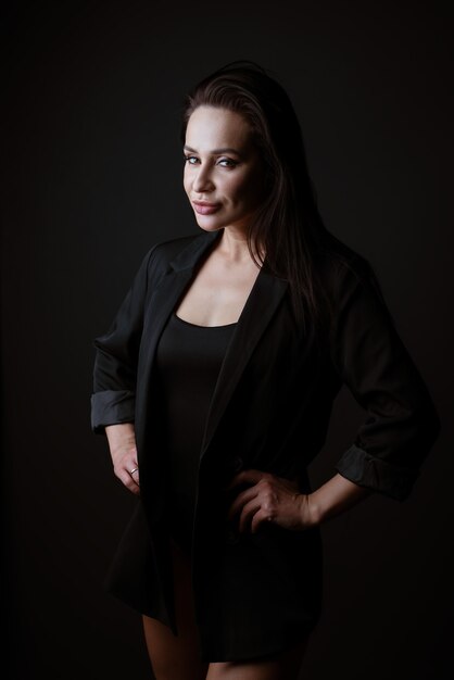 Portrait of a beautiful woman in a black bodysuit and jacket posing on a dark background