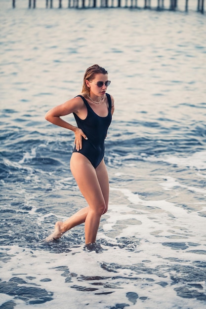 Portrait of a beautiful woman in a black swimsuit with blond hair posing on the beach by the sea Young woman walking on the beach