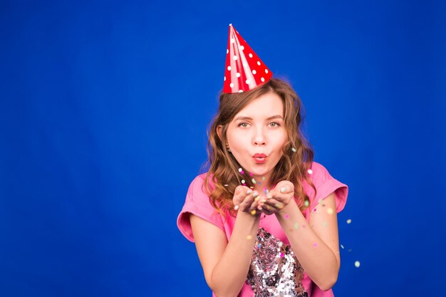 Portrait of beautiful woman blowing confetti in the air party new years eve celebration on blue background