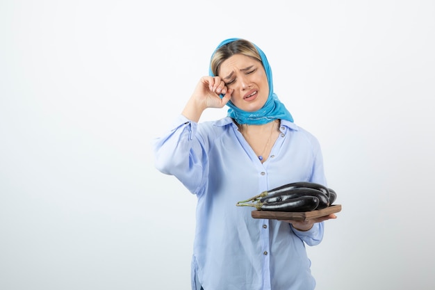 Portrait of beautiful woman in blue shawl holding eggplants with sad expression