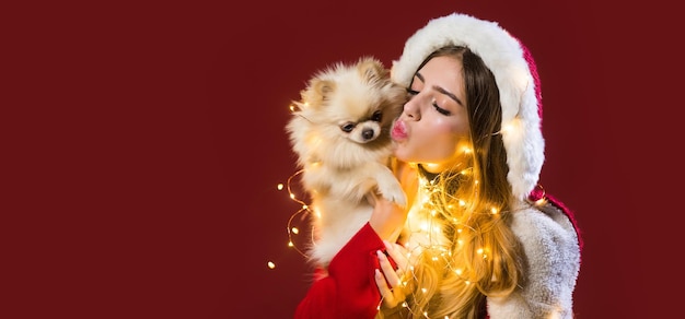 冬のクリスマス休暇を祝う美しい女性の肖像画は、赤の背景に子犬を保持します