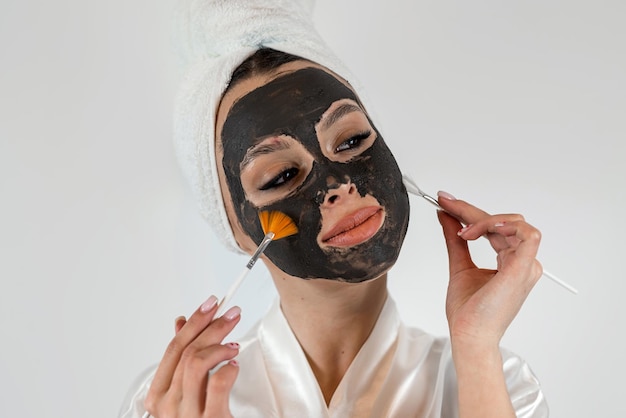 Portrait of beautiful woman doing beauty treatments use clay mask and hold brush isolated on white