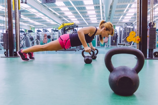 Portrait of beautiful woman doing pushups over black iron kettlebells in a crossfit training on fitness center