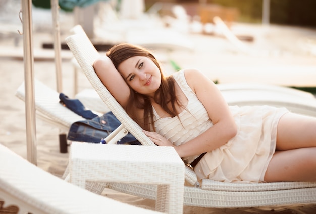 Portrait of beautiful woman in dress lying on sunbed at beach