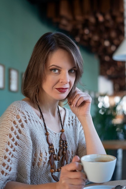 Portrait of beautiful woman drinks coffee on inside cafe
portrait of brunette girl sits at table in cafe