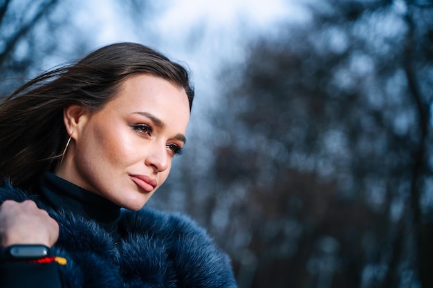 Portrait of a beautiful woman in an elegant fur coat attractive lady Dark hair Blurred park background