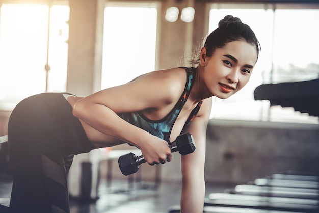 Photo portrait of beautiful woman exercising with dumbbell in gym