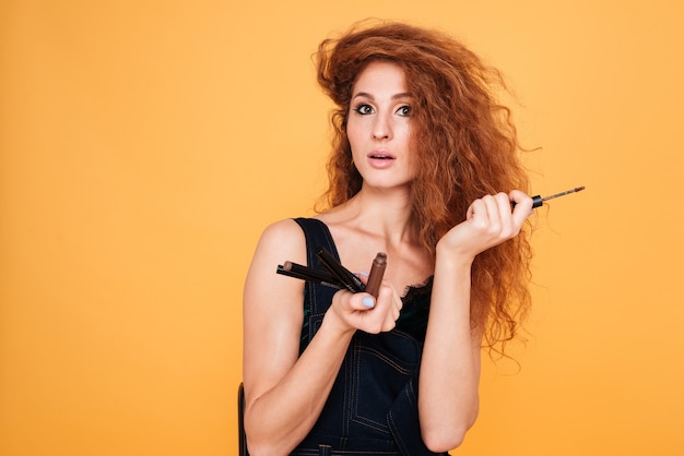 Portrait of a beautiful woman holding different lip glosses for makeup isolated on orange