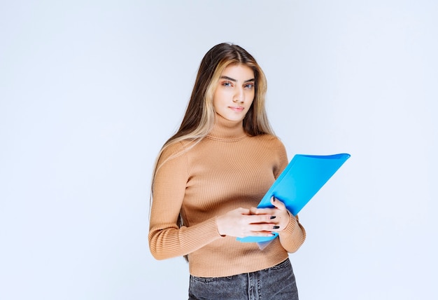 Portrait of a beautiful woman holding a folder against white wall .