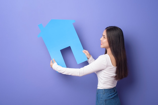 Portrait of beautiful woman is holding blue home on purple\
background