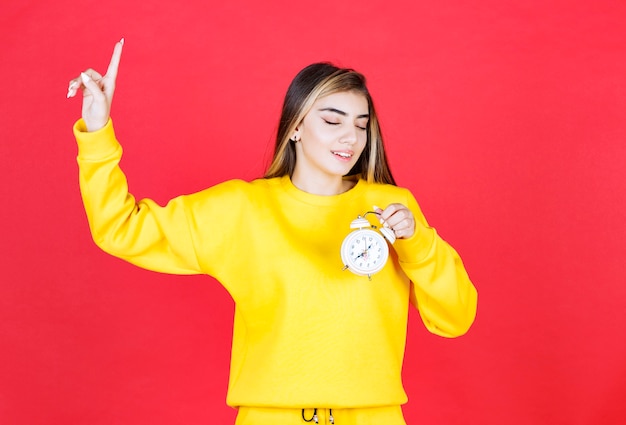 Portrait of beautiful woman looking at time on clock on red wall