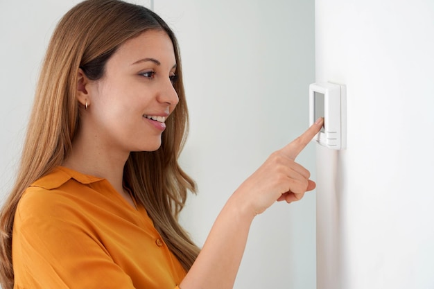 portrait of beautiful woman lowering the temperature for energy saving woman adjusting digital central heating thermostat at home