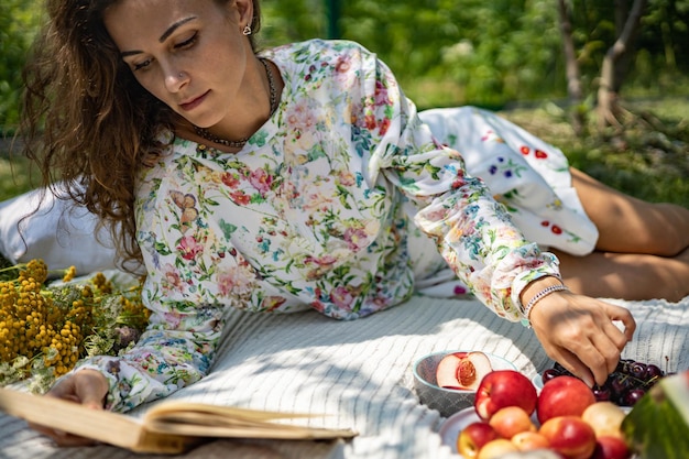 Ritratto di bella donna in posa sdraiato sul plaid al parco giardino estivo un libro frutta una borsa e un wat