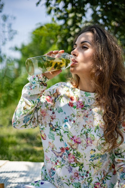 Ritratto di bella donna in posa sdraiato sul plaid al parco giardino estivo un libro frutta una borsa e un wat